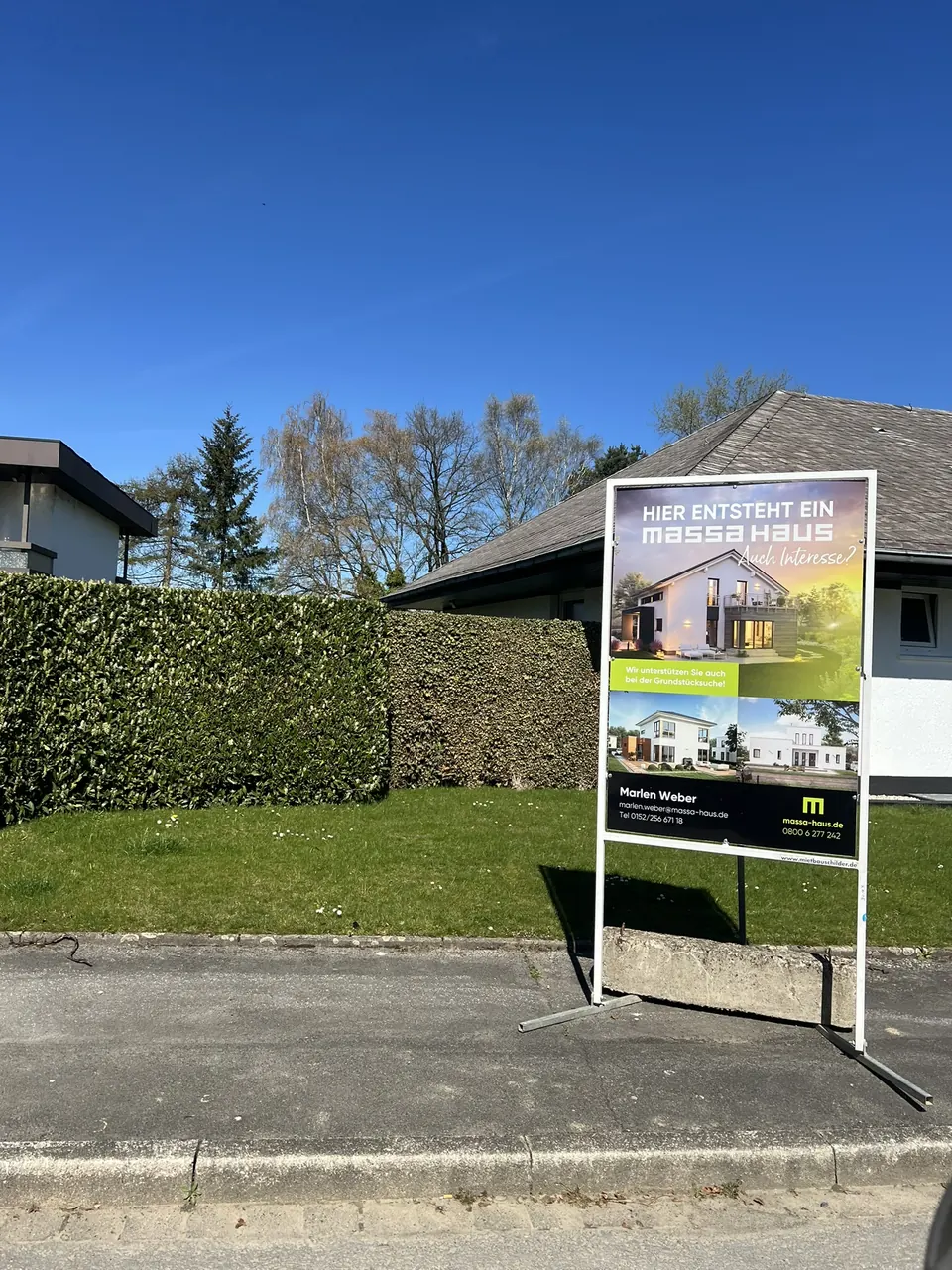 Bauschild „Hier entsteht ein massa haus“ vor einer Hecke in Schwerte
